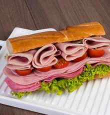 Delicious stacked ham and salami sandwich with lettuce and tomatoes on a tray.